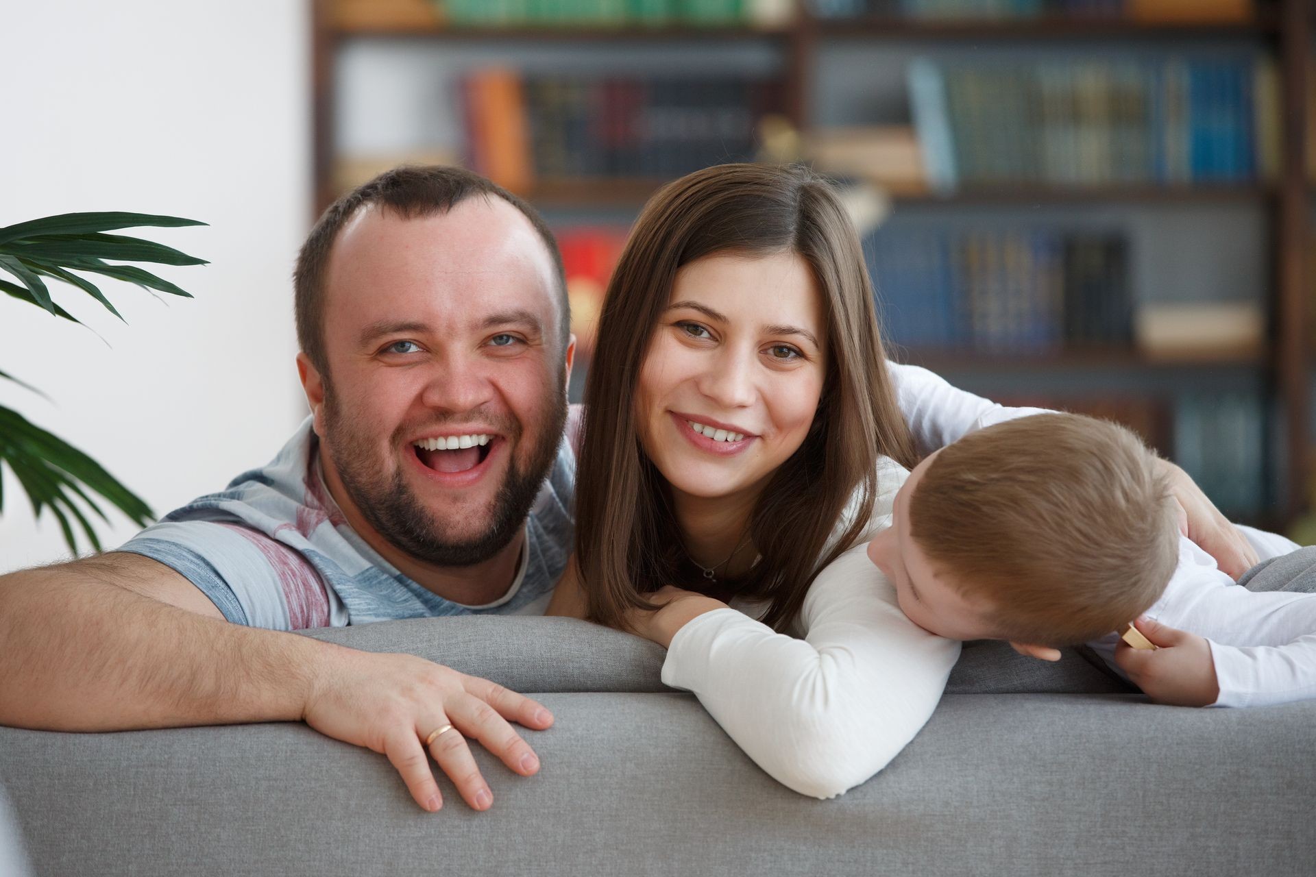 Image of smiling family with son sitting on gray sofa